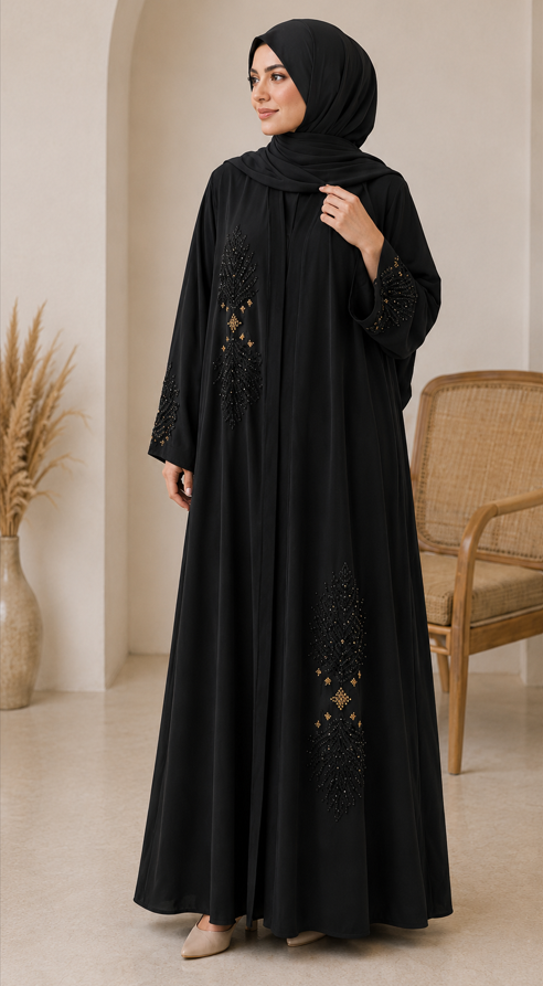 Woman wearing a black abaya with intricate designs in a room with a beige wall and wooden chair.