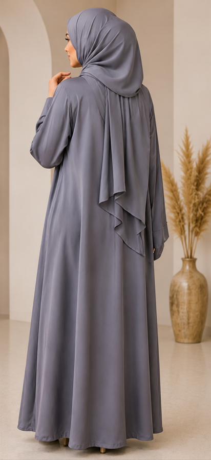 Woman wearing a gray abaya in a room with a vase and dried plants.
