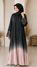 Woman wearing a black and pink gradient dress with embroidery in an indoor setting.